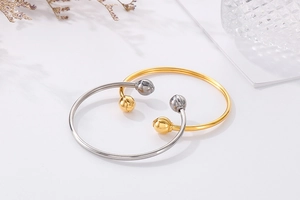 Minimalist open gold and silver stainless steel bangles with ball ends on white surface