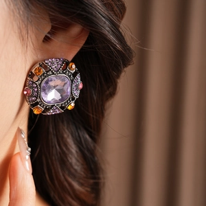 Close-up of vintage square earrings with purple stones and colorful diamonds on ear