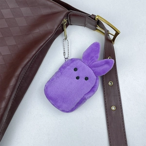 Detail of purple plush rabbit keychain attached to a brown leather bag with a bead chain