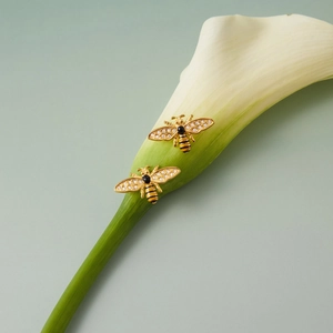 Detailaufnahme von goldenem Bienenschmuck mit Emaille und Kristallen auf Lilie