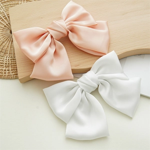 Detailed view of large pink and white satin bow hair clips on a wooden textured background