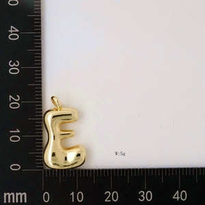 Macro shot of gold letter E bubble pendant measuring 22mm on a scale ruler, weight 5g
