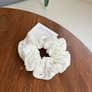Detail of white pleated lace scrunchie with oval bow patch on a dark wood tray