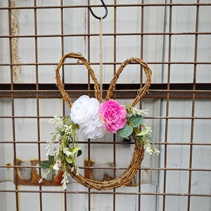 Detail of bunny wreath made of natural dry rattan with realistic flowers and metal hook