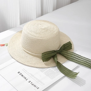 Detail of a chic raffia sun hat featuring a green ribbon bow and pearl bead decoration