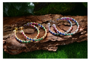 Macro detail of large C-shaped gold earrings with colorful pear-cut zircon on tree bark