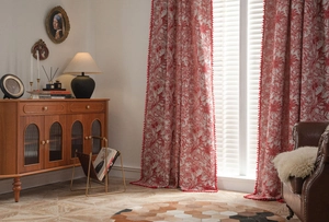 Detail of red floral curtains with plush pom-pom trim and elegant fabric drape