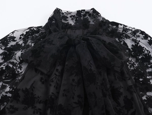 Close-up of the black sheer mesh neckline featuring floral flocking and an elegant bow tie