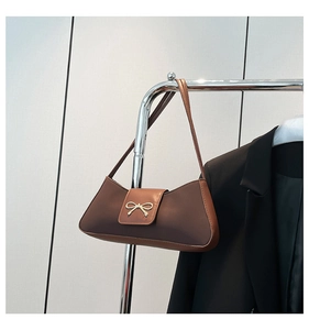 Detailed view of a brown faux leather shoulder bag featuring a gold bow accent on a hanger