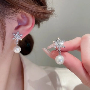 Detailed view of silver snowflake earrings with sparkling diamonds and round white pearls