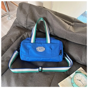 Blue nylon sports bag with TOCHASO embroidery and striped handles on a grey sofa