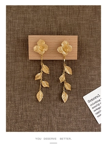 Détail de boucles d'oreilles pendantes à fleurs et feuilles dorées sur support en bois