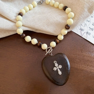 Gros plan d'un pendentif coeur en bois avec croix argentée sur un collier ethnique