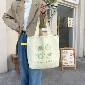 Detail of cute apple embroidery and drawstring closure on creamy yellow canvas tote bag