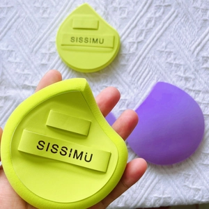 Close-up of green and purple teardrop makeup sponges with SISSIMU logo on soft fabric