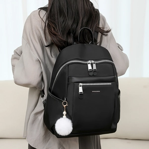 Minimalist black nylon backpack for women with white pompom pendant in home setting