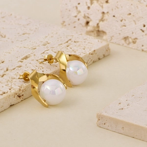 Close-up of golden pearl earrings with iridescent luster on a textured stone surface