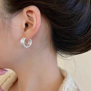 Close-up of a matte silver C-shaped chunky hoop earring worn on model's ear