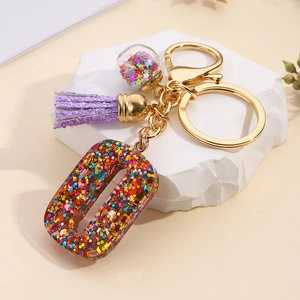 Macro view of a resin letter O keychain with colorful sequins and a purple tassel charm