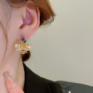 Close-up of elegant gold bee earrings with yellow stones and crystals on model ear