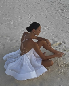 Detail of white backless dress featuring thin cross straps and a voluminous pleated skirt