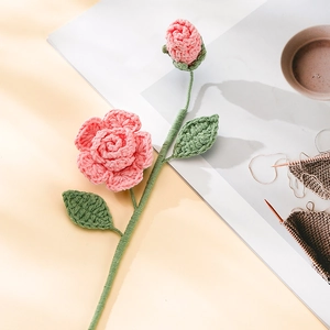 Close-up of handmade crochet rose with pink petals and green leaves on beige paper