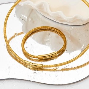 Minimalist gold snake chain necklace set with sleek cylindrical clasp on a mirrored surface
