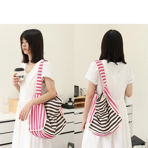 Modella mostra il fronte e il retro di una grande borsa a tracolla in tela a righe