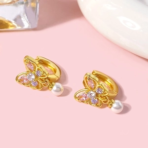 Détail macro de boucle d'oreille papillon dorée avec zircons colorés et perle