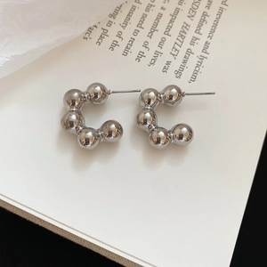 Detailed close-up of silver C-shaped beaded metal earrings on a minimalist book background