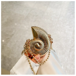 Detailed view of a golden seashell evening bag with metallic texture and beaded chain