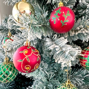 Detail of red and gold faceted Christmas balls hanging on a white flocked tree branch