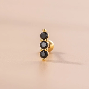 Close-up of golden cartilage stud earring with three vertical black zircon stones