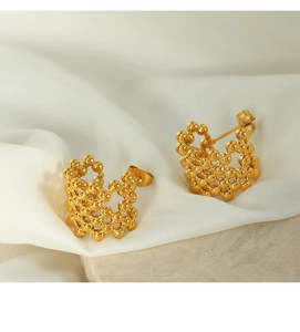 Macro detail of 18K gold plated mesh C-shaped ball earrings on white silk fabric