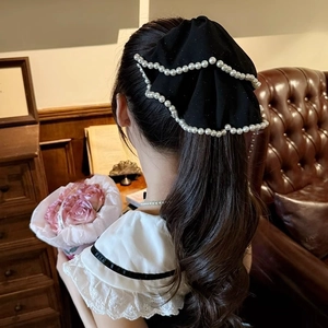 Elegant black bow hair clip with pearl edges worn by a model in a cozy home setting