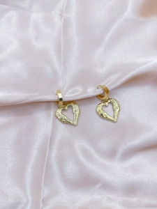 Detailed view of gold heart-shaped earrings with textured wing patterns on pink silk
