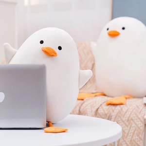 Detail of soft white plush duck doll on a desk with laptop in cozy home setting