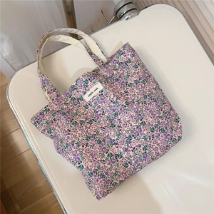 Detail view of purple floral cotton tote bag with white woven label on white surface