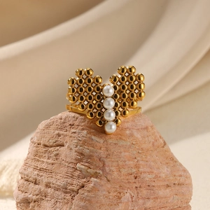 Close-up of golden pearl ring with butterfly design on a coral rock background