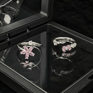 Macro detail of silver open rings with pink zircon flowers and stones on a black mirror