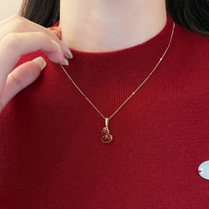 Détail du pendentif gourde dorée avec pierre rouge et zircons sur un pull