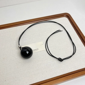 Close-up of a long minimalist necklace with a glossy black spherical pendant and wax cord