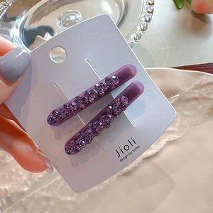 Detailed macro of two purple rhinestone hair clips on a white display card holder