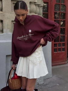 Vintage burgundy half-zip sweatshirt with chest logo, styled with a white pleated skirt