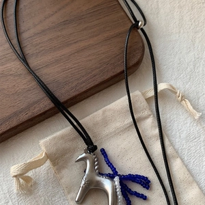 Macro view of silver pony pendant with blue beaded tassels on a black wax rope chain