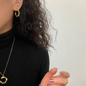 Close-up of a model wearing minimalist twisted gold hoop earrings and a curved necklace