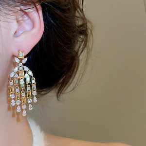 Close-up of elegant gold tassel earrings with yellow and clear zircon stones on a model