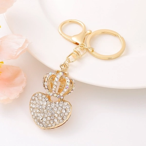 Close-up of golden heart and crown keychain with sparkling rhinestones on white tray