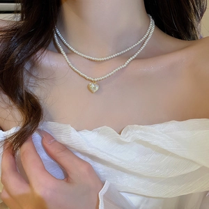 Detail of double-layer pearl necklace with a gold-bordered heart pendant on neck