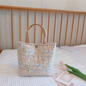 Floral quilted lunch bag with beige straps and metal buckle in a cozy home setting